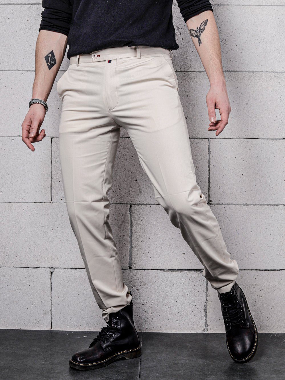 A man in VANILLA PANTS is leaning against a brick wall.