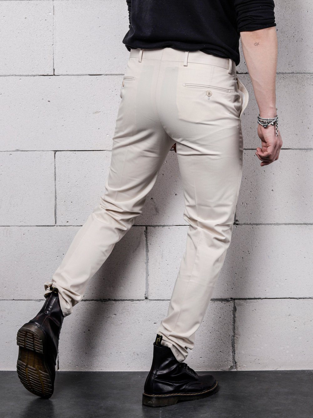 A man is standing against a brick wall wearing vanilla pants.