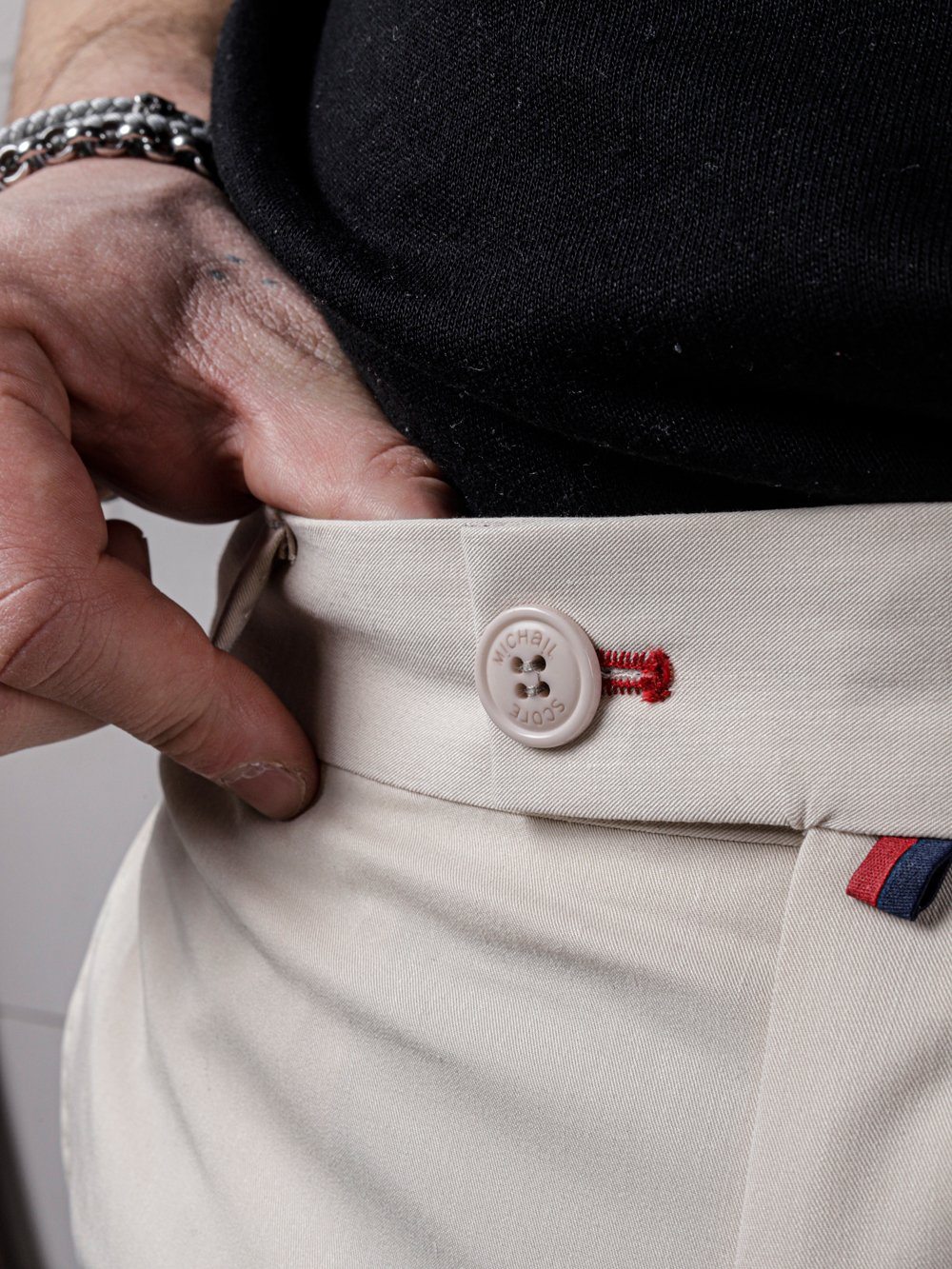 A man is holding a button on his VANILLA PANTS in beige color by SERNES STREETWEAR