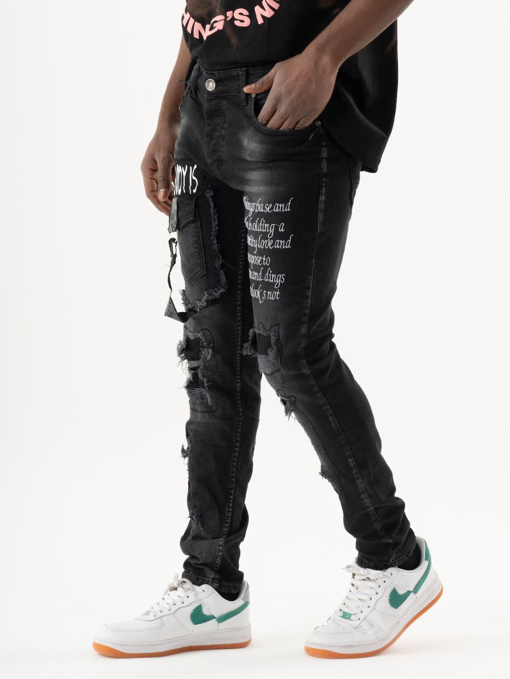 A man wearing black ripped jeans and a black ONE SOUL t - shirt.
