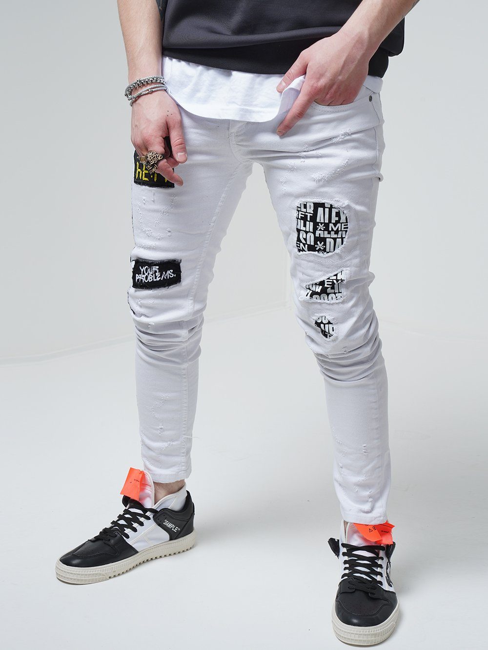 A man wearing WHITE FALCON jeans with patches on them.
