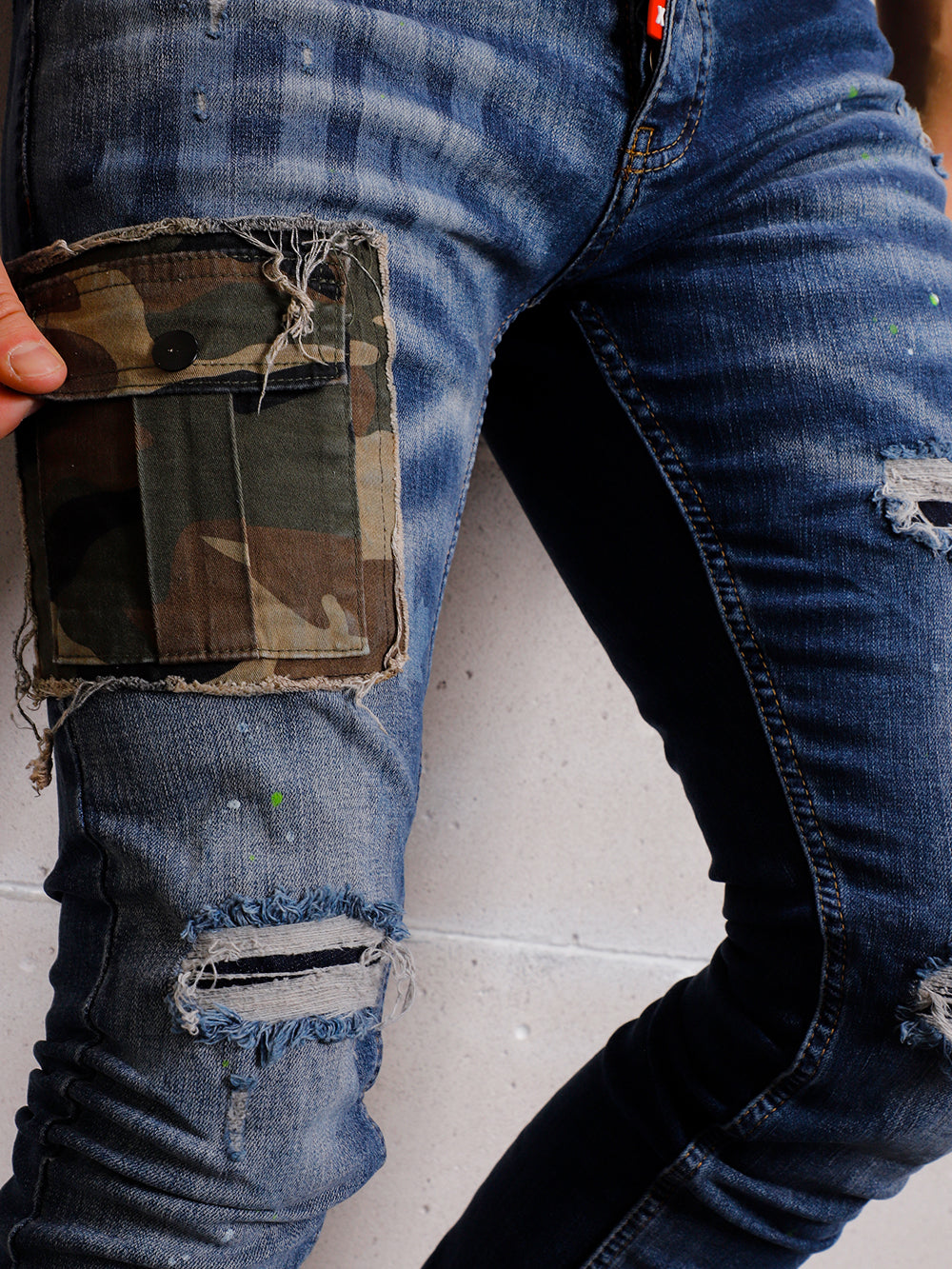 A man wearing ripped jeans with a BLUE CAMOUFLAGE pocket.