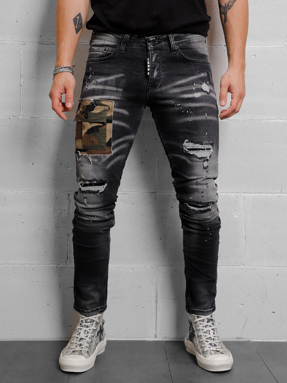 A man wearing ripped jeans and a CAMOUFLAGE | BLACK t - shirt.