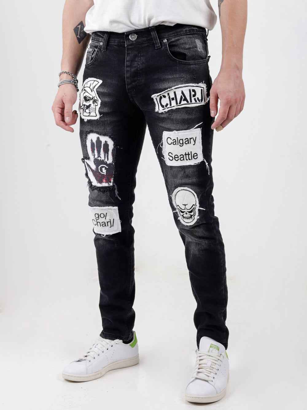 A man wearing BLACK HEADSTONE jeans with patches on them.
