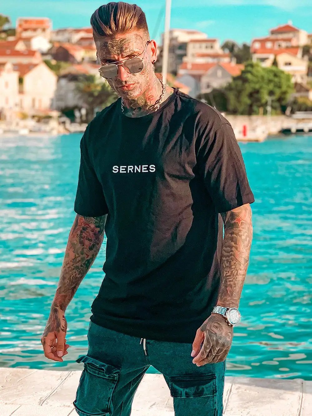 A man wearing THE ORIGINAL T-SHIRT standing next to the water.