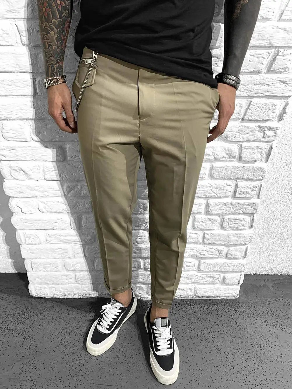 A man with hand crafted tattoos and khaki pants is standing next to a GENTLEMAN'S ROLL UP - BEIGE.